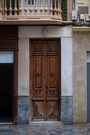 Rustic wooden door with a marble doorframe and stone balcony overhead