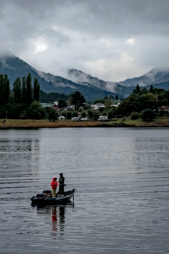 A couple fishing from a small boat in front of cloudy mountains